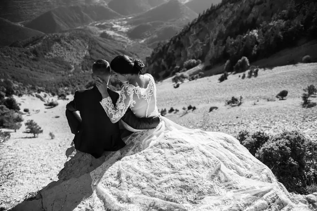 Photo en noir et blanc d'un couple de mariés assis enlacés sur un rocher