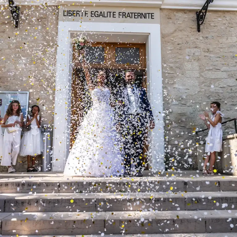 Sortie triomphale des mariés de la mairie française sous une pluie de confettis dorés et blancs
